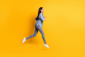 Fototapeta na wymiar Full size profile photo of cool optimistic brunette lady go run wear blue shirt jeans sneakers isolated on yellow color background