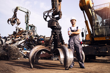 Portrait of worker standing by hydraulic industrial machine with claw attachment used for lifting...