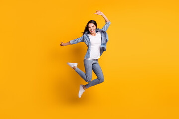 Full size profile photo of cool optimistic brunette lady jump wear blue shirt jeans sneakers isolated on yellow background