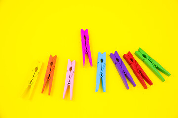 Colorful wooden clothespins on yellow background. Close up, copy space. Minimalism, original and creative photo. Be another. Individuality concept.
