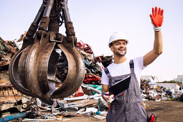 Junkyard worker waving to the crane operator to start lifting scrap metal parts.
