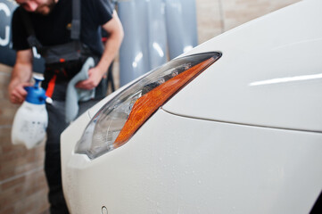 Worker in detailing garage put polyurethane anti-gravel film cover in white luxury car.