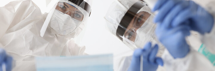 Doctors in protective suits putting mask on patient and measuring temperature