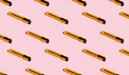 Stationery knives on a pink background, pattern, hard shadows. Construction tools, repairs. Background for the design.