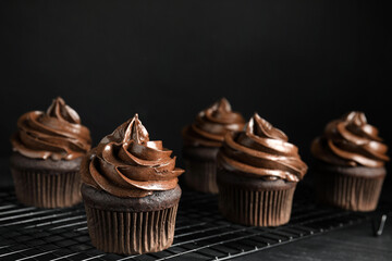 Cooling rack with delicious chocolate cupcakes on black table against dark background. Space for...