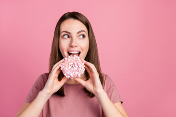 Portrait of attractive funny cheerful hungry girl eating biting fresh doughnut isolated over pink...
