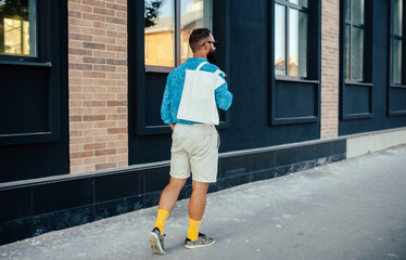 Street portrait of young stylish hipster man with white blank textile eco shopping bag or tote bag. Mock up for design