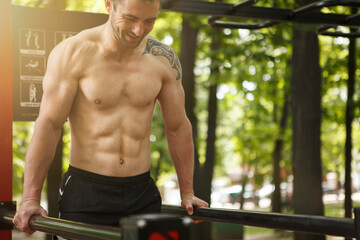 Cropped shot of a sportsman smiling, enjoying working out in the forest, doing triceps dips