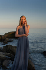 Fototapeta na wymiar beautiful girl in a gray dress by the sea at sunset