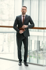 Portrait of confident young businessman in suit looking at camera while standing at office corridor