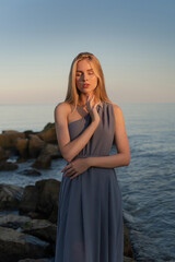 beautiful girl in a gray dress by the sea at sunset