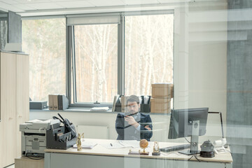 Image of businessman sitting at the table and working at office behind the glass wall
