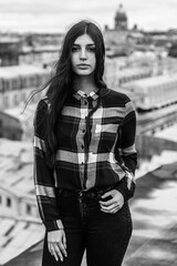 An Armenian girl with long black hair in a plaid shirt stands on a rooftop in the center of St. Petersburg