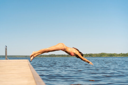 Woman jumping into the lake from wooden pier. Having fun on summer day on the vacations. Young girl diving in to the water from the dock.