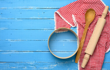 wooden rolling pin, round wooden sieve on blue background with red napkin