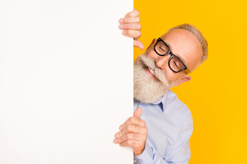Photo of cheerful positive happy old man look empty space blank board isolated on yellow color...