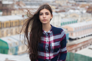 Obraz premium portrait of an Armenian girl with fluttering long black hair in a checkered shirt and jeans on a rooftop in the center of St. Petersburg
