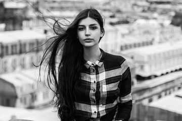 portrait of an Armenian girl with fluttering long black hair in a checkered shirt and jeans on a rooftop in the center of St. Petersburg