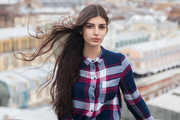 portrait of an Armenian girl with fluttering long black hair in a checkered shirt and jeans on a rooftop in the center of St. Petersburg