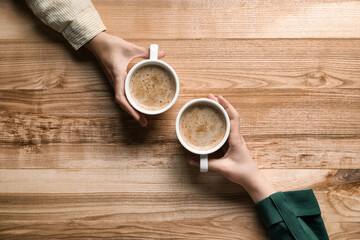 Women with cups of coffee at wooden table, top view