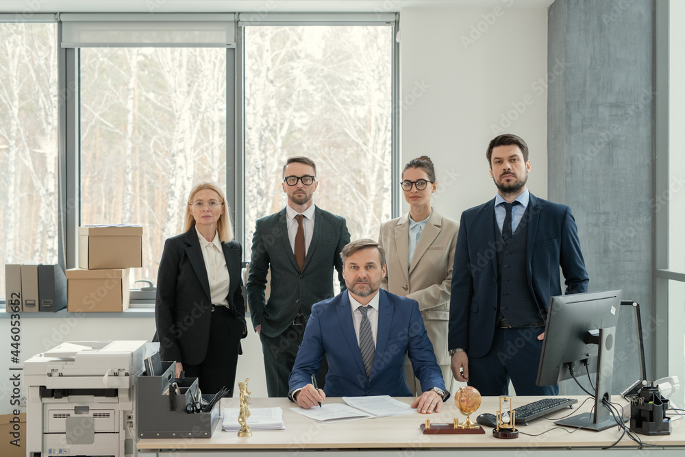 Poster portrait of group of business people looking at camera while standing at office with their leader in