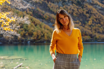 Portrait of smiling woman at crystal lake in the autumnal mountains.