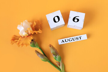 Calendar for August 6 : the name of the month of August in English, cubes with the numbers 0 and 6, yellow iris on a yellow background, top view