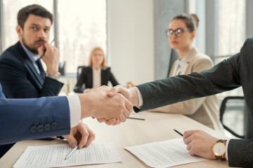 Close-up of business people shaking hands while sitting at the table during a meeting at office