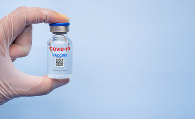 Hand holding of a COVID-19 vaccine bottle with a light blue background. Vaccine for immunization, and treatment from coronavirus infection. Close-up photo. Healthcare and medical concept