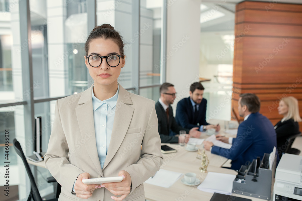 Poster portrait of young businesswoman in eyeglasses looking at camera while using digital tablet with her 