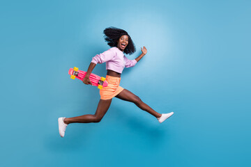 Fototapeta na wymiar Full size photo of young happy crazy afro girl with brunet hair running in air with skate isolated on blue color background