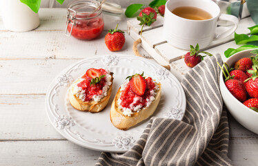 Homemade bruschetta with cottage cheese and strawberries for breakfast at white wooden background