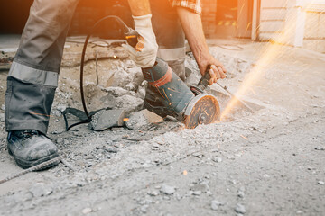 A worker with a grinder cuts the concrete pavement of the road and sparks fly. Construction and...