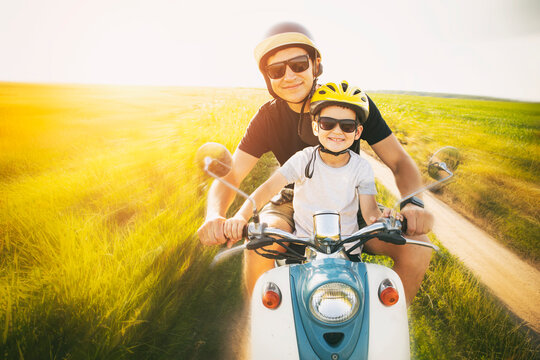 The father and son riding together through the field by pathway on the retro scooter - Powered by Adobe