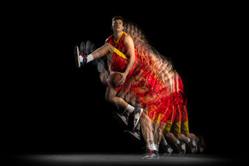 Portrait of young basketball player training with ball isolated on dark background with stroboscope...