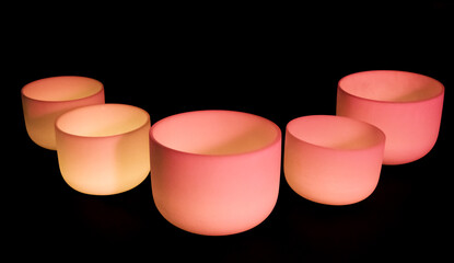 Crystal singing bowls with pink light on a dark background
