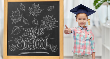education, learning and people concept - happy little student girl with in bachelor hat or...