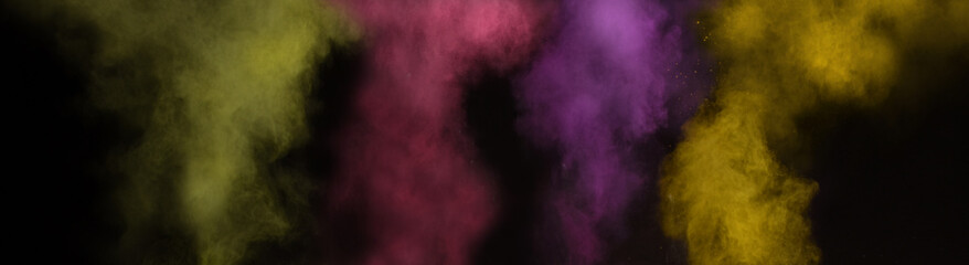 Beautiful explosive background of holi powders with yellow magenta violet and green colors flying over a black background