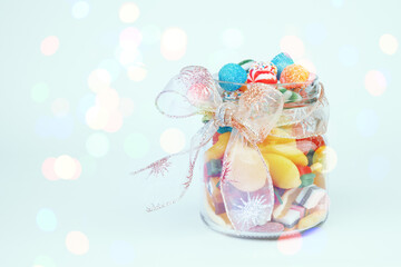 Fototapeta na wymiar Jar of various sweets decorated with a bow. Glowing lights on the background. Festive concept.