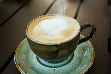 Sugar is poured into a cup of cappuccino. Cappuccino in a beautiful gray-green clay gull