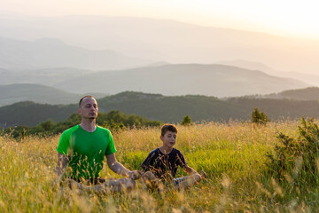 Fototapeta na wymiar Single father and son doing yoga exercises on grass in nature at the sunset. People having fun outdoors. Concept of friendly family and of summer vacation.