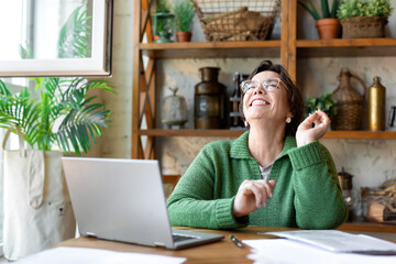 Happy laughing senior woman in front of laptop monitor. She sitting in home interior and having online conversation with relatives or friends. - obrazy, fototapety, plakaty