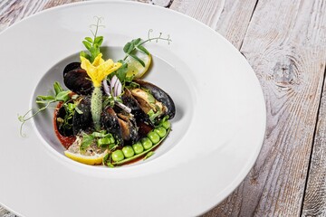 Close-up of mussels with green peas and gherkins in wine sauce on a white plate. Healthy and delicious traditional mediterranean seafood. Restaurant recipe. Copy space