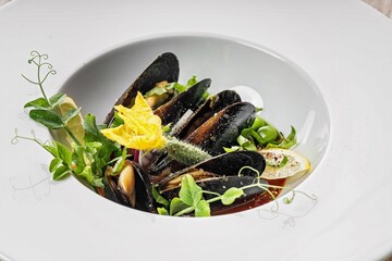 Close-up of mussels with green peas and gherkins in wine sauce on a white plate. Healthy and...
