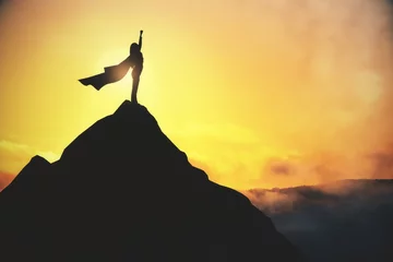 Foto op Canvas Success and satisfaction concept with super woman in waving coat on top of dark rock on yellow foggy sky background. © Who is Danny