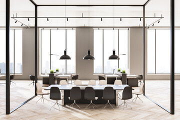 Front view on meeting table in conference room with glass walls in spacious sunny office hall with modern interior design, black vintage lamps and city view from huge windows