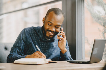 Man sitting in a cafe and working behind a laptop, writing in a notebook.