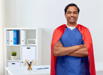 healthcare, profession and medicine concept - happy smiling indian doctor or male nurse in blue uniform and red superhero cape over medical office at hospital background