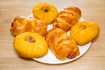 Belyashi with meat and sausages in a delicious yellow dough on a white round plate on a wooden board background. Bakery products national traditional dishes and pastries.