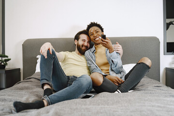 Multiracial pair watching tv together in bed